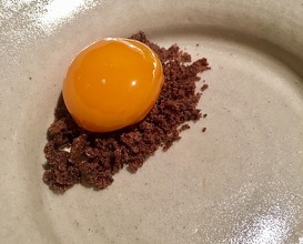 An egg yolk preserved in sugar syrup served on a pile of crumbs made from pine tree bark